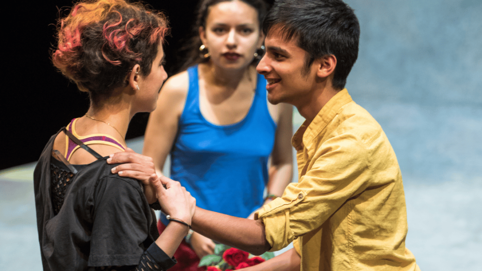 A young man talking to a woman with his hand on her shoulder. A young woman looking on in the background.