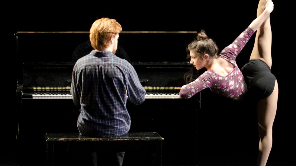 A dancer leaning on the piano with their leg in the air, and a musician playing the piano with their back to the camera