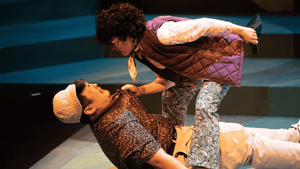 A man is on the ground, standing over him is a woman pulling him up by the collar. 