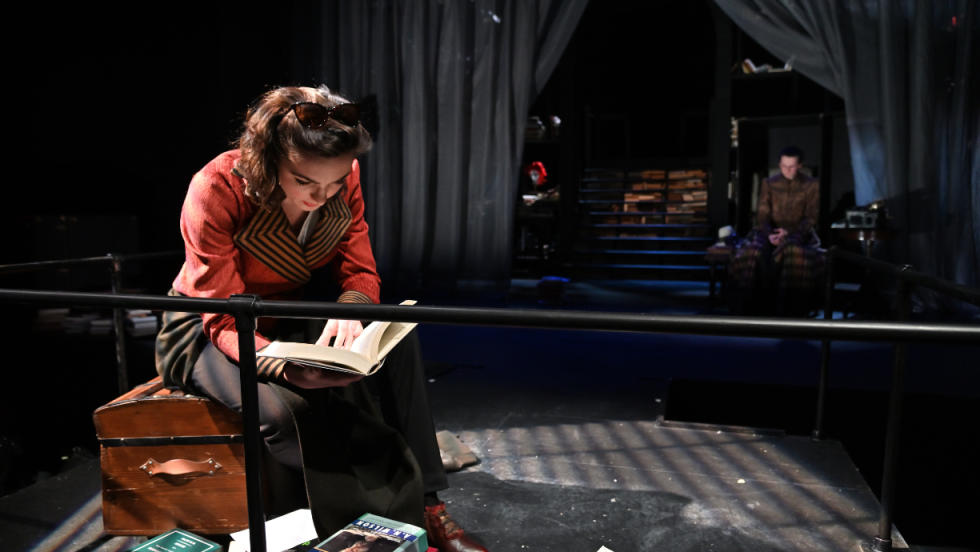 A woman sitting on a trunk, bent over, and reading a book. 