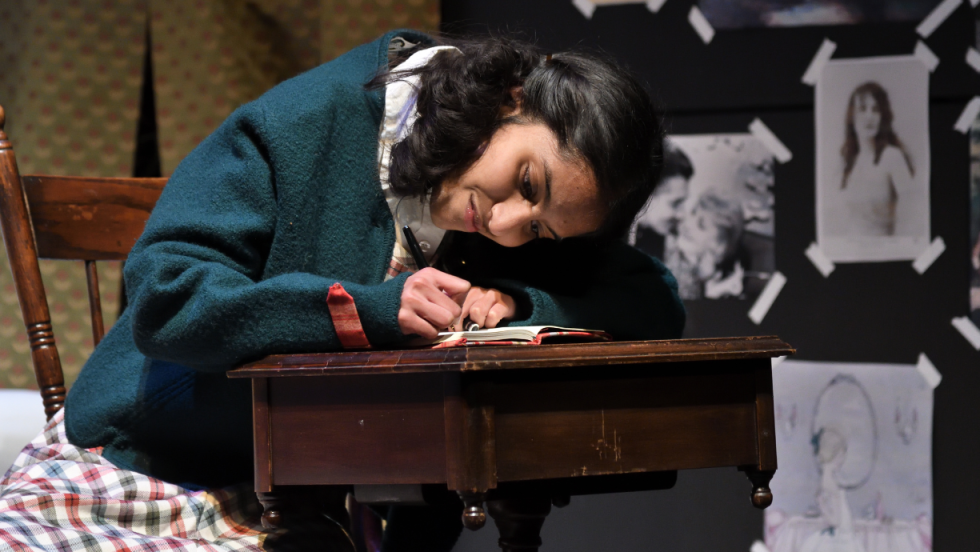 Young woman sitting down bent over a desk and writing in a notebook. 