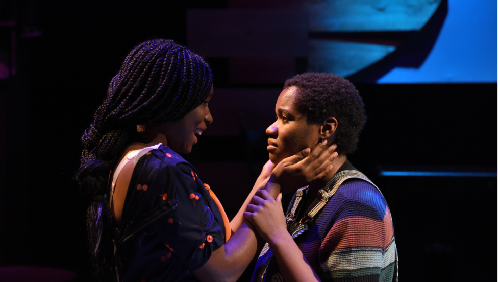 Two women looking at each other, one of the women is holding the other woman's face in her hands. 