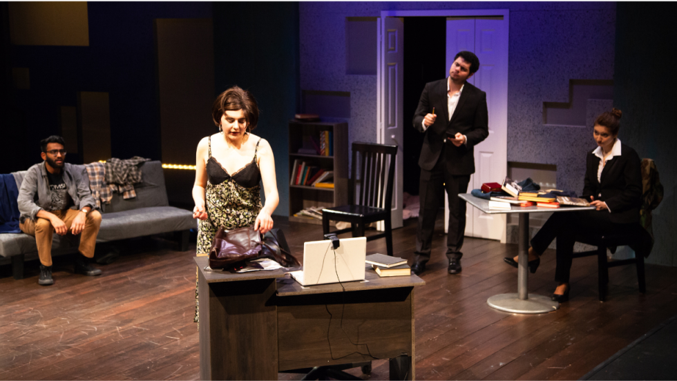 A woman reaching for a bag on a table. 3 men in the background, looking at her. 