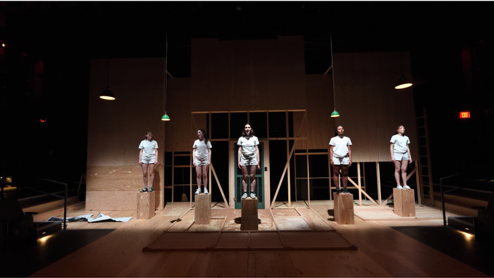 5 young women standing on wooden blocks with the spotlight on them. 