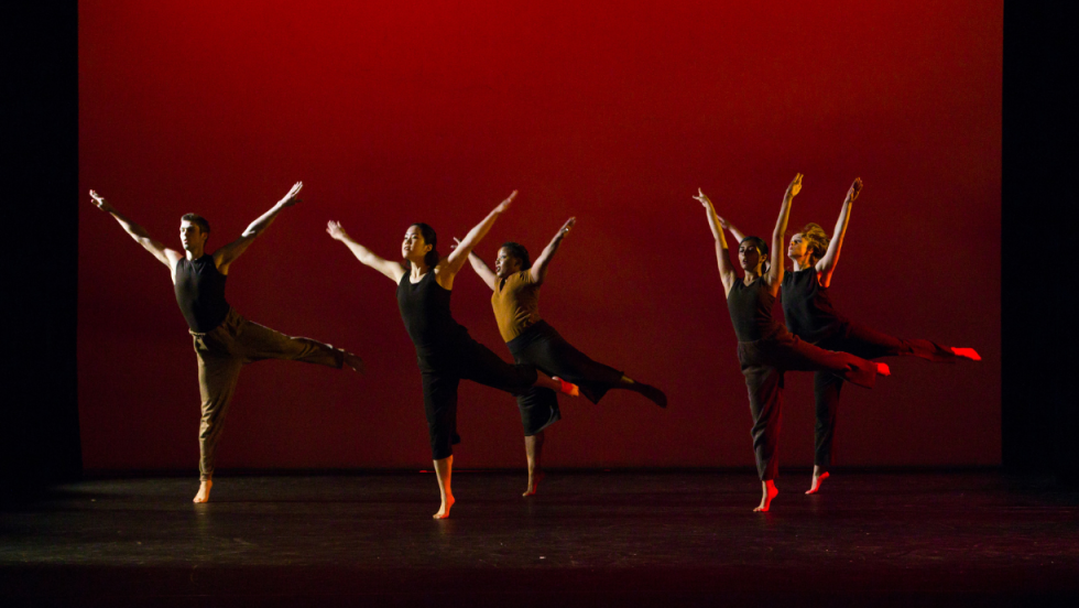 Five female dancers dancing together with arms stretched upwards. 