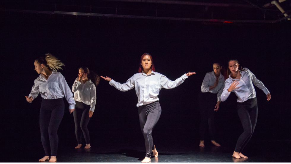 A group of young women dancing, one woman in the center with her arms stretched out sideways 