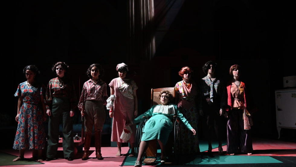 8 women standing shoulder to shoulder, one of the women is in a wheelchair, dead.