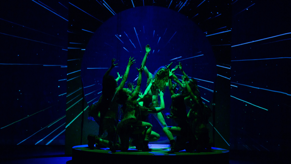 A group of dancers flocking around a singular dancer in center stage 