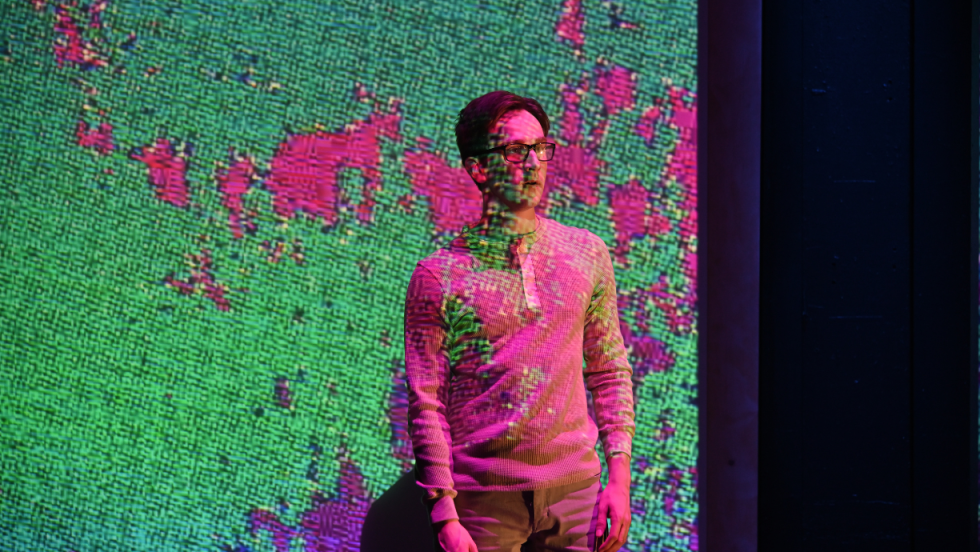A young man with pink and green projections reflecting on him. 