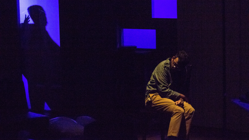 A man sitting by himself, on a dimly lit stage.