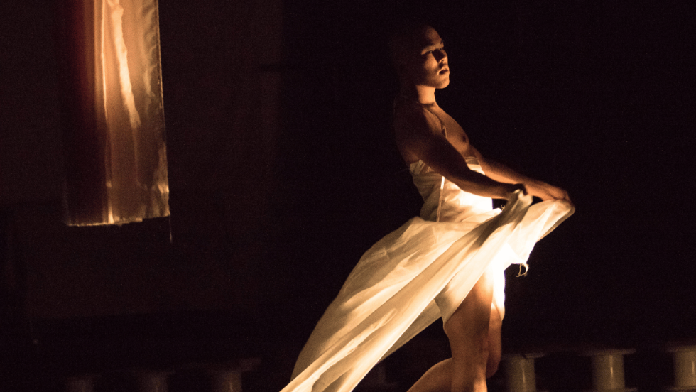 A man draped in sheer white fabric about the waist in dim lighting 