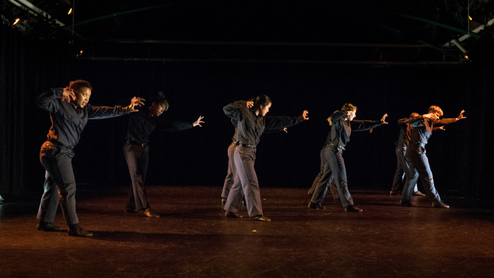 A group of dancers wearing black dancing with arms up 