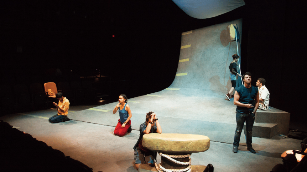 A group of people dispersed around a stage and a climbing wall in the background. 